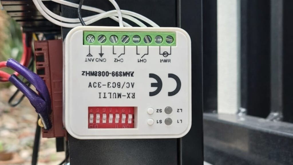 Close-up of aftermarket gate receiver module with wiring terminals and dip switches installed on motor