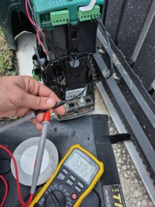 Technician testing voltage on sliding gate motor using multimeter for diagnostics